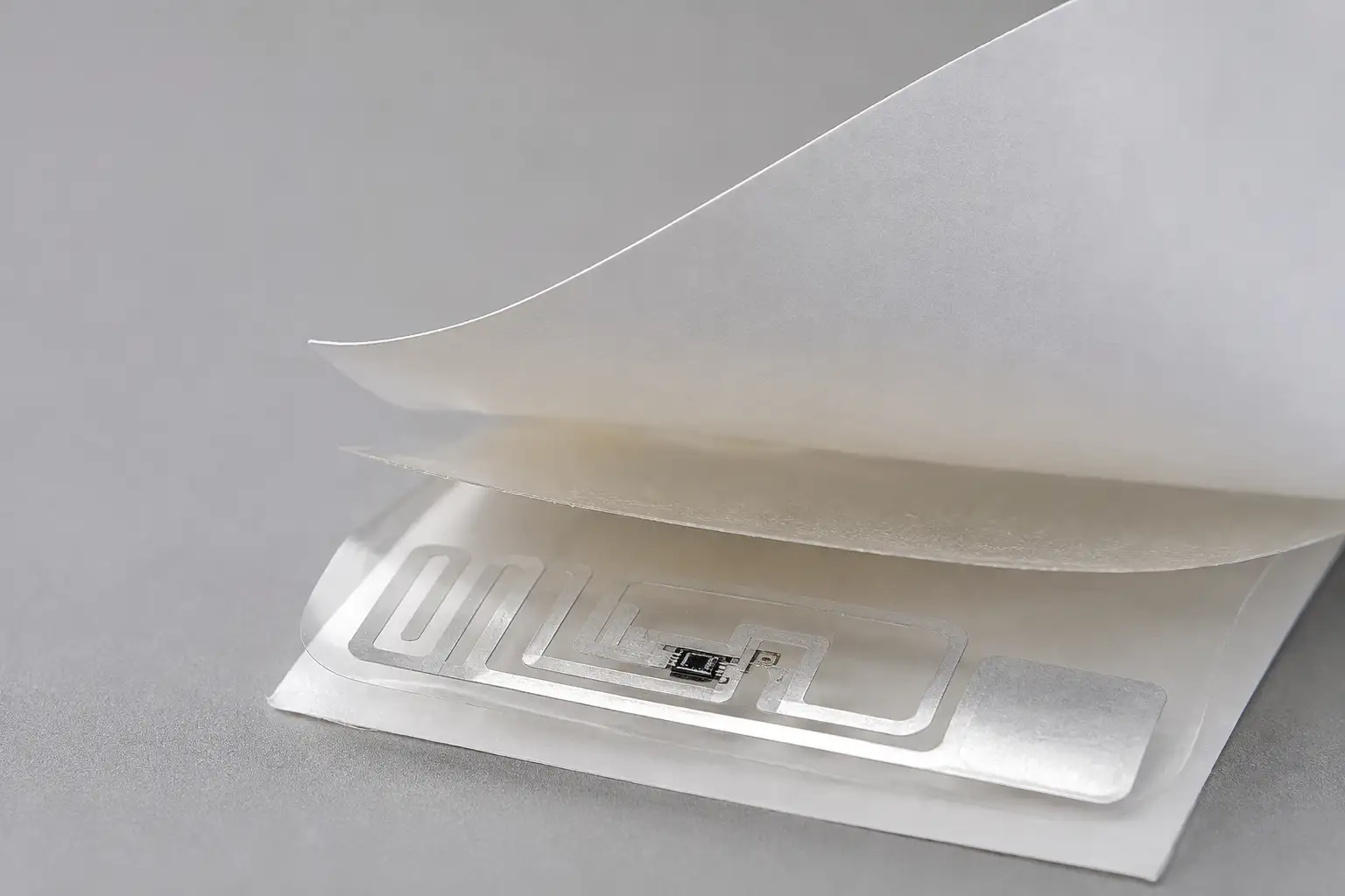 Close-up of Hy paper printable RFID label peeled back to show embedded UHF RFID inlay and chip.
